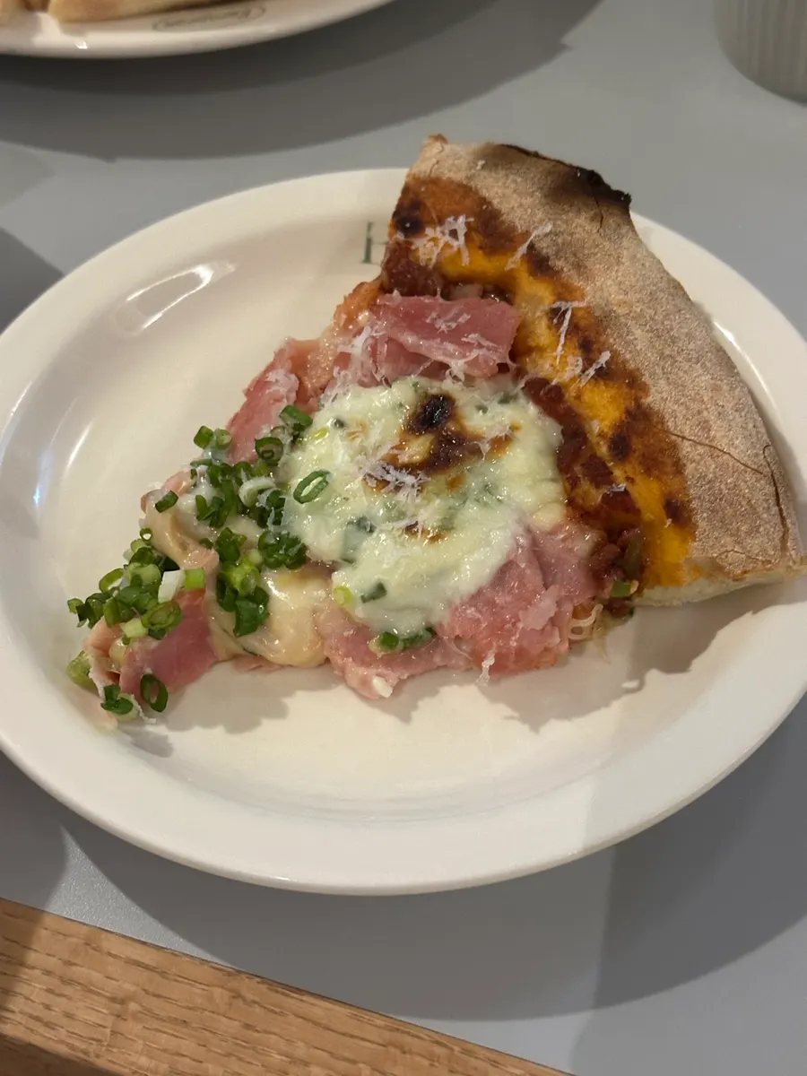 A slice of pizza topped with green onion and jambon
