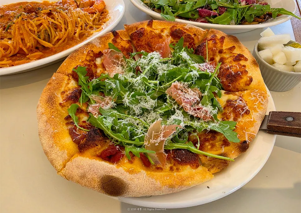 Wood-fired pizza topped with arugula and prosciutto