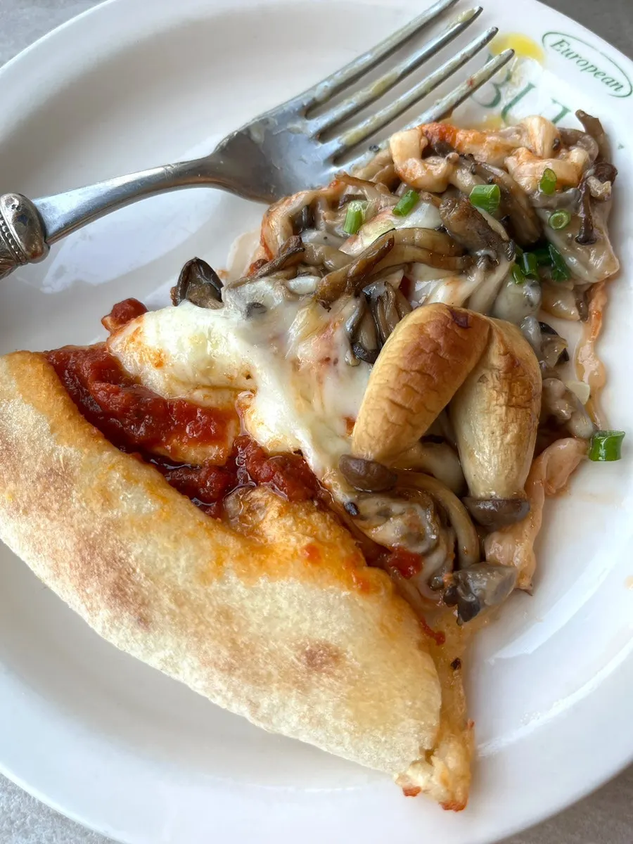 A slice of mushroom pizza drizzled with Tabasco sauce