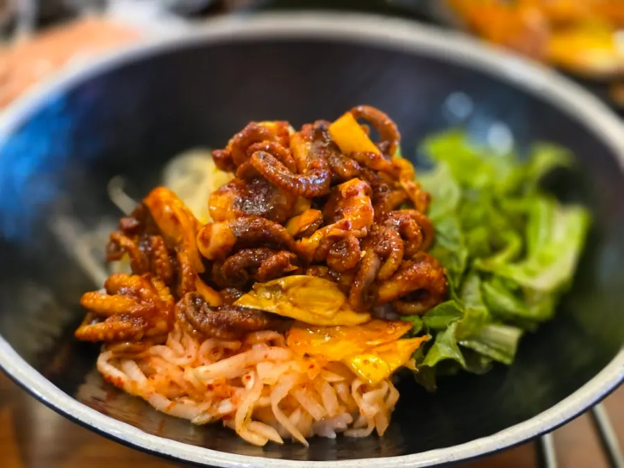 Mixing vegetables and jjukkumi stir-fry together in a bowl