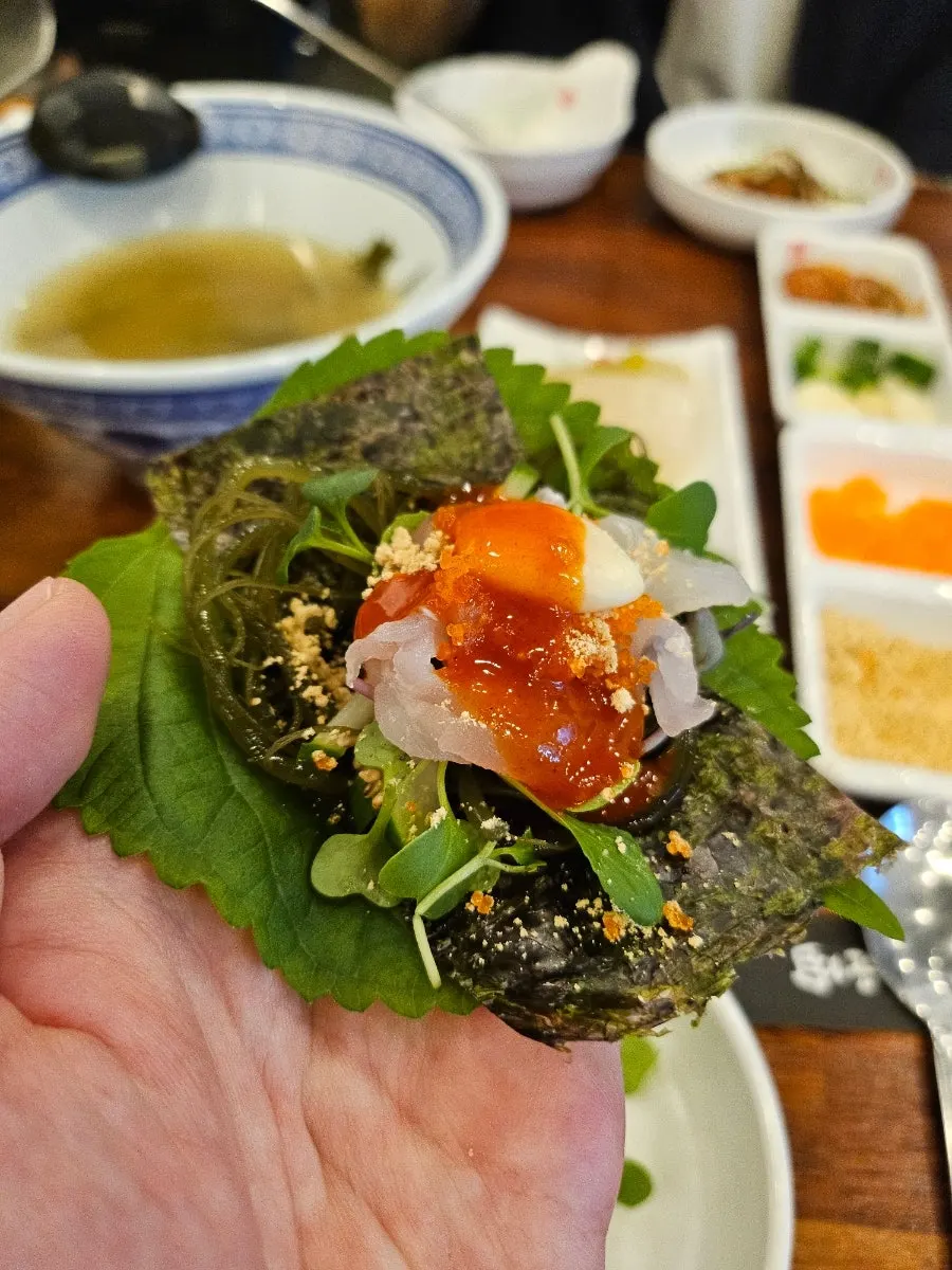 A makhoe wrap on perilla leaf topped with gim and gijeli seaweed