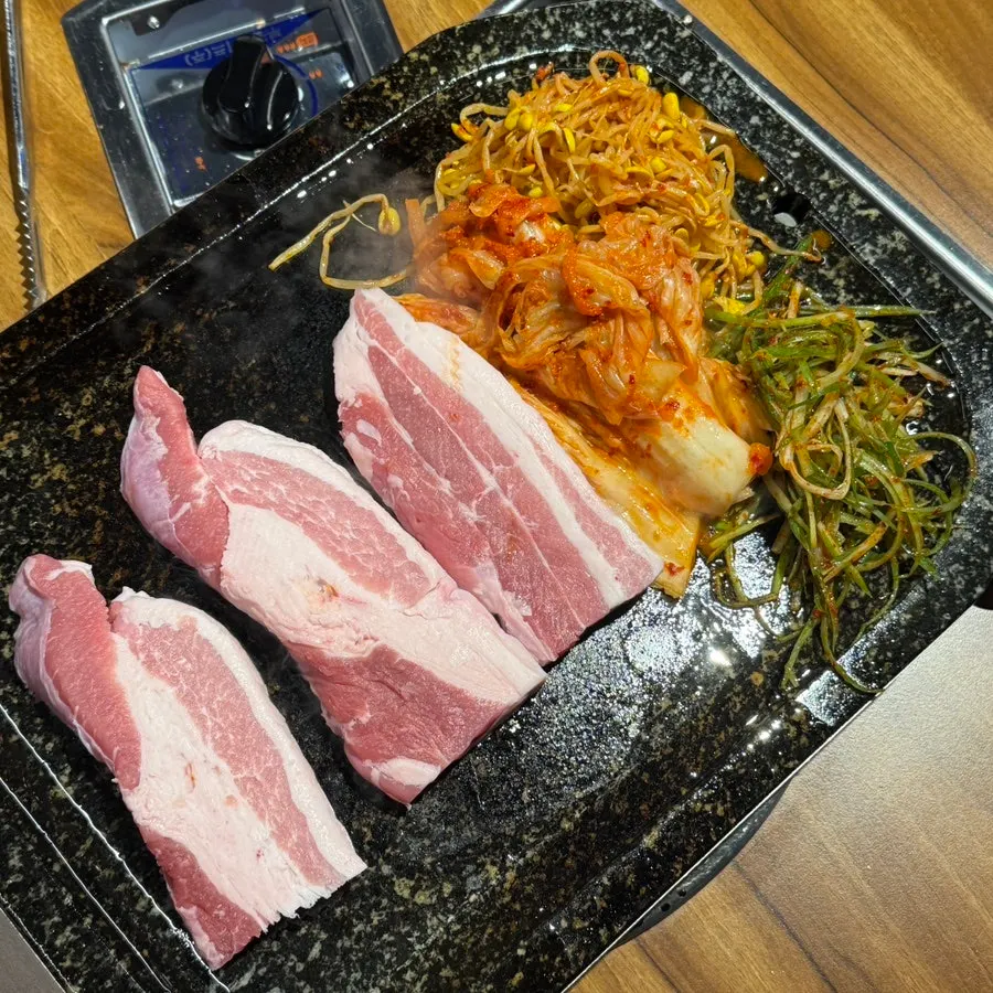 Fresh pork belly on the stone plate with scallion strips, seasoned bean sprouts, and kimchi