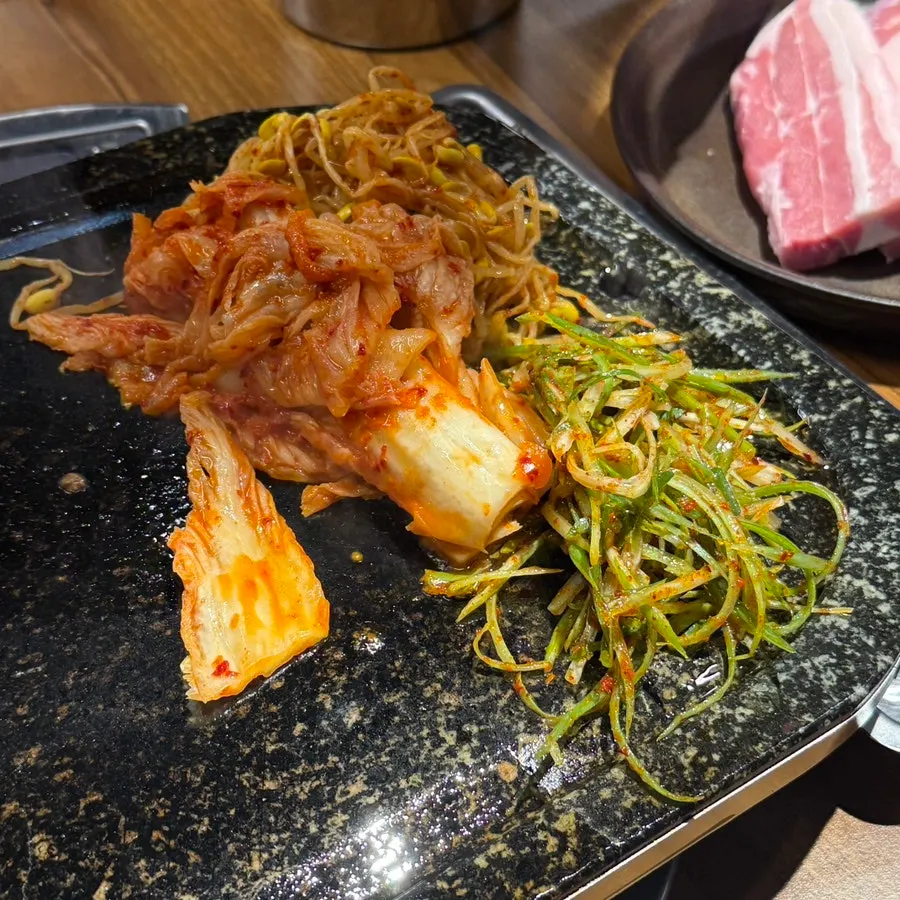Kimchi, bean sprouts, and scallion strips cooking together on the grill plate