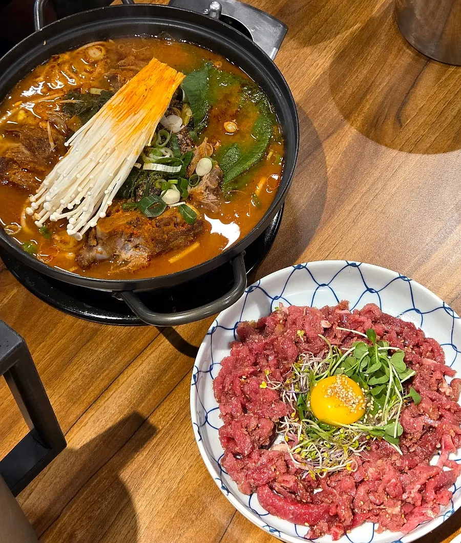 Table with gamjatang, beef tartare and pork belly laid out together