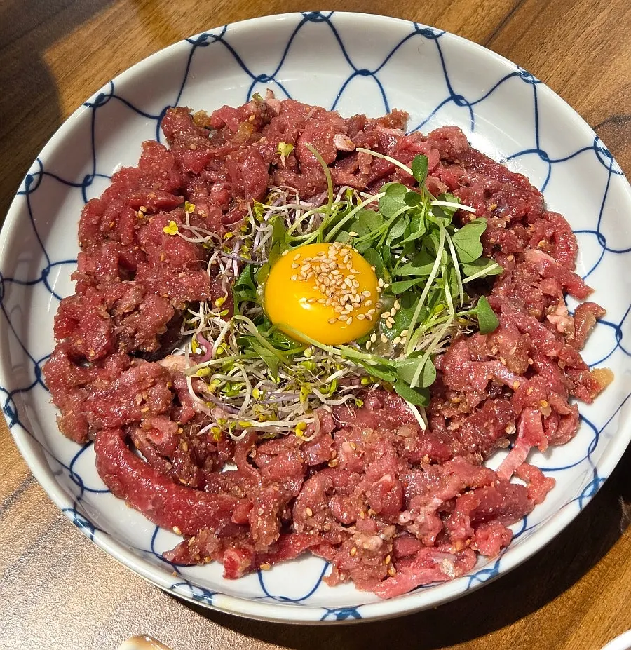 Beef tartare topped with egg yolk and sprouts