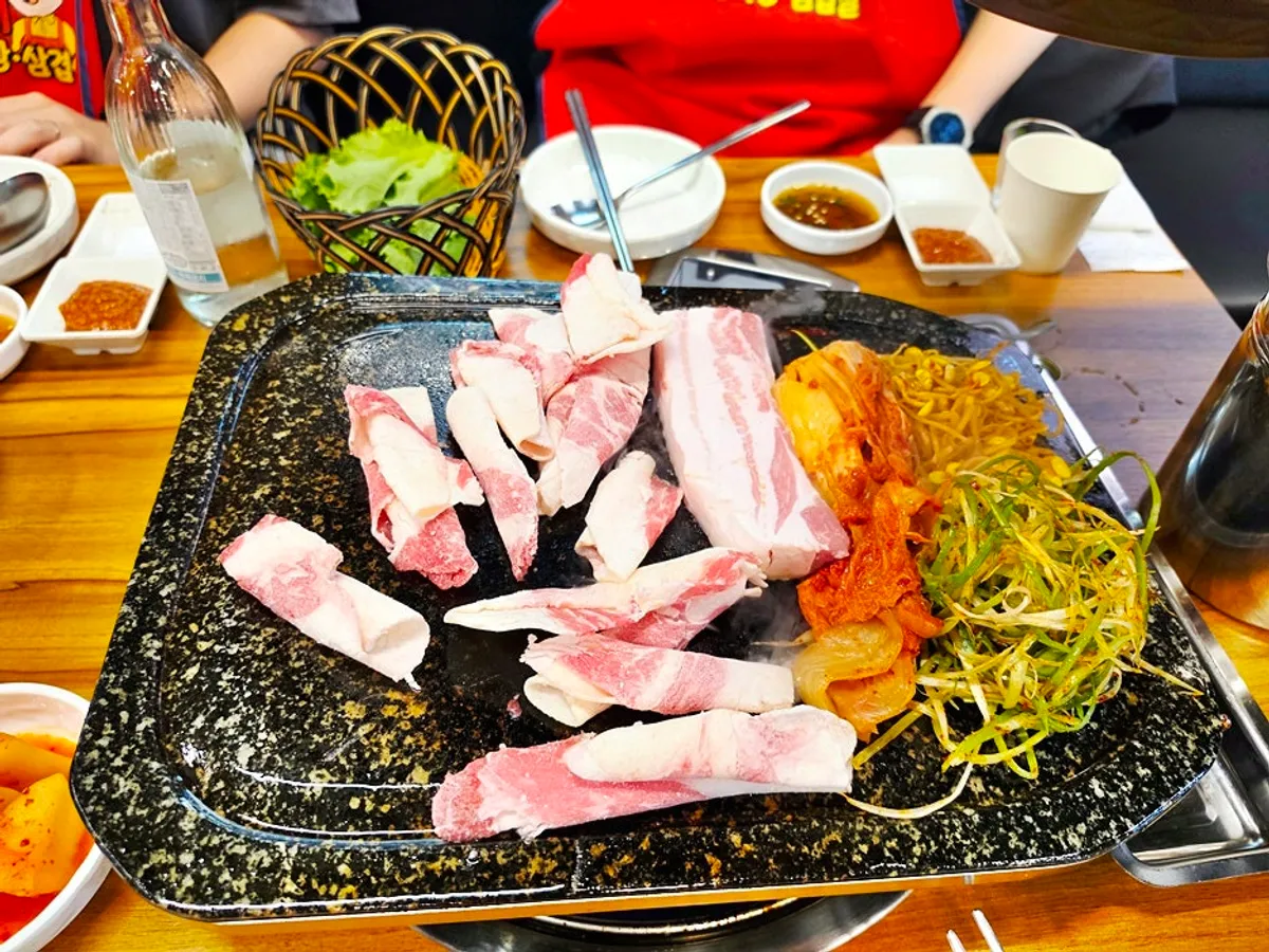 Meat grilling alongside bean sprouts, scallions, and kimchi