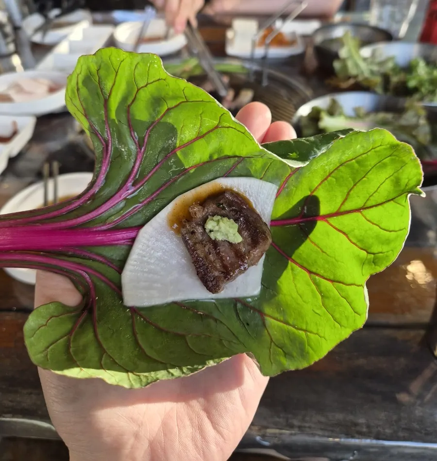 A wrap of ssam greens with meat and wasabi