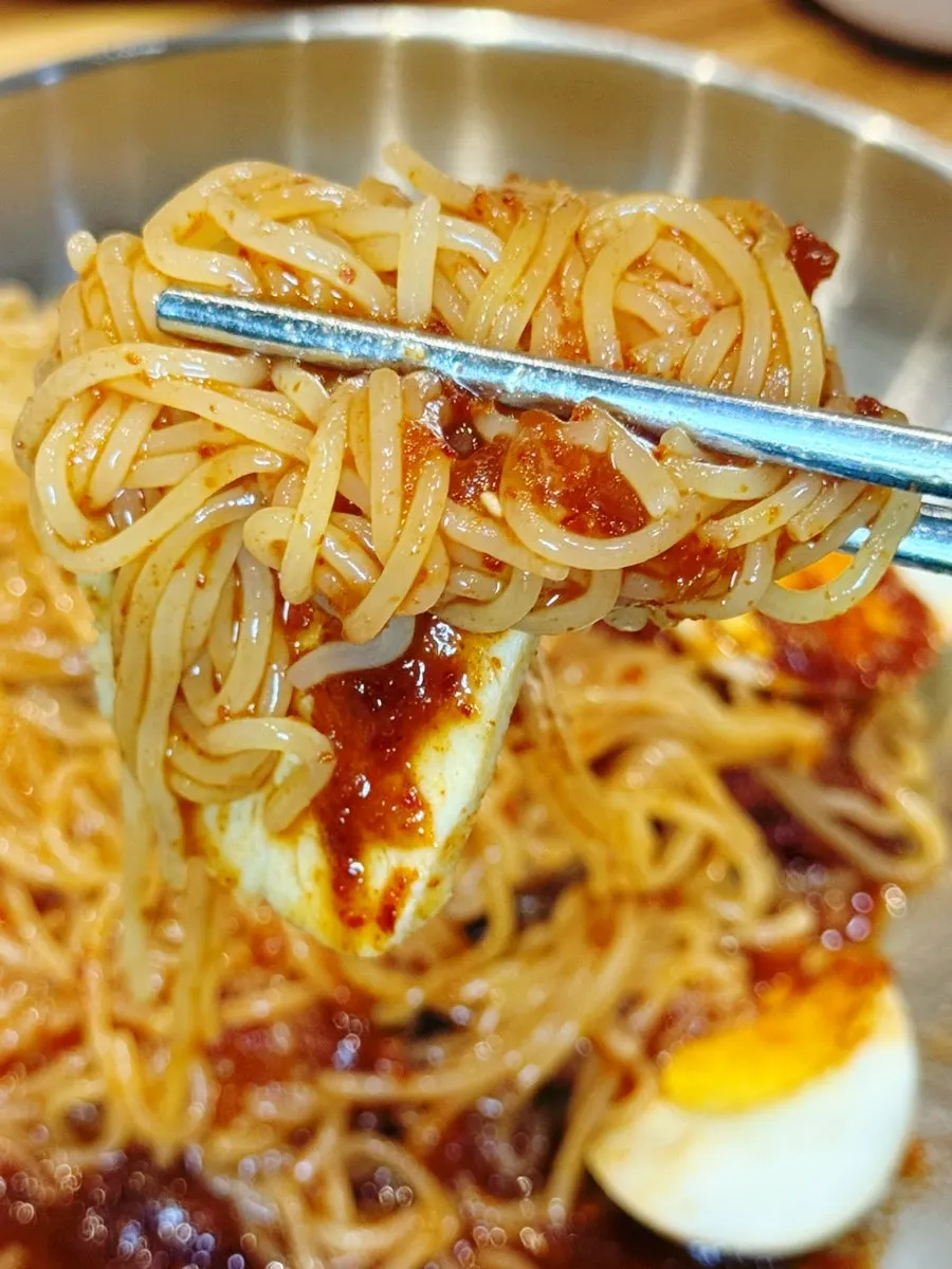 A bite of bibim milmyeon paired with boiled pork