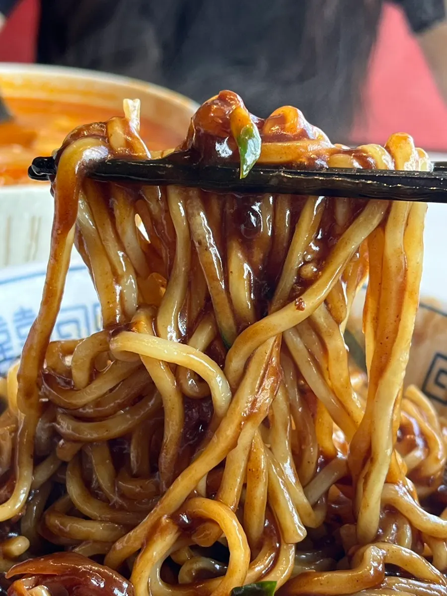 Chopsticks lifting a bite of jjajangmyeon noodles