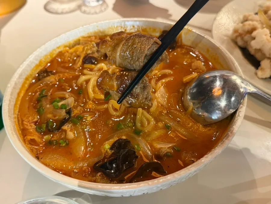 Spicy jjamppong broth and ingredients lifted with a spoon