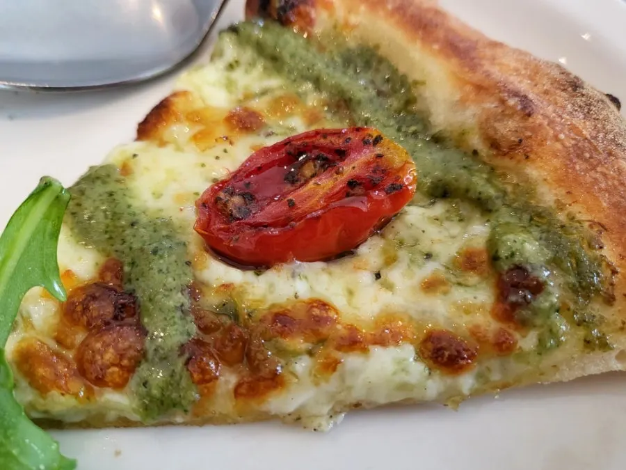 A slice of pizza showing the basil pesto base