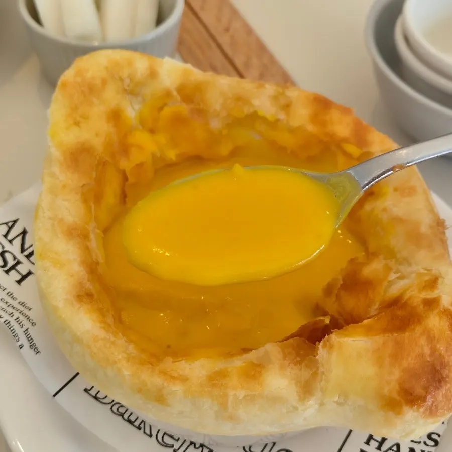 Pastry cracked open with a spoon over pumpkin soup