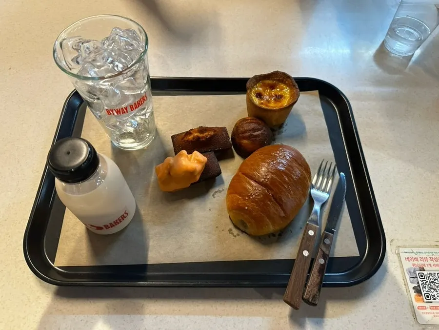 Tray loaded with salt bread, financiers, egg tart, butter rice cake, and milk tea