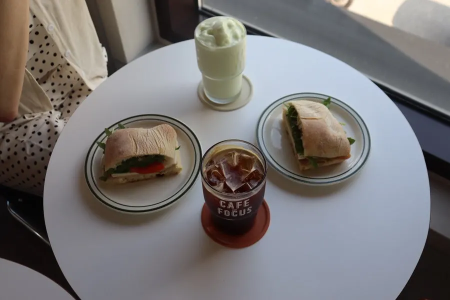 Table setting with ciabatta sandwich, avocado smoothie, and Americano