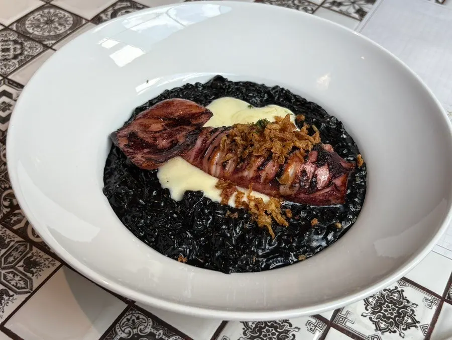 A plate of squid ink risotto topped with whole squid
