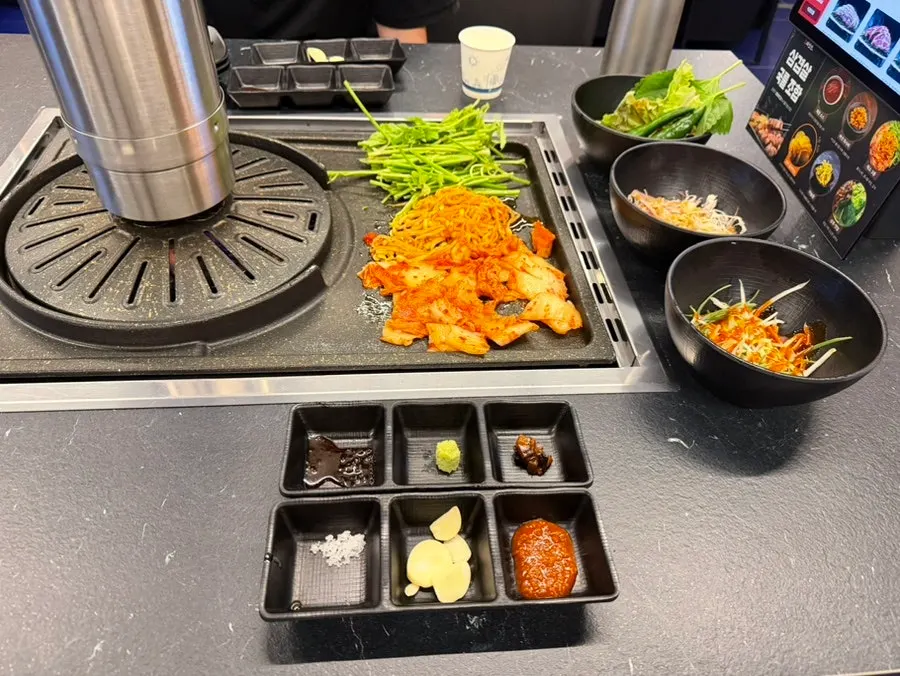 Kimchi, bean sprouts, and minari grilling alongside the pork belly