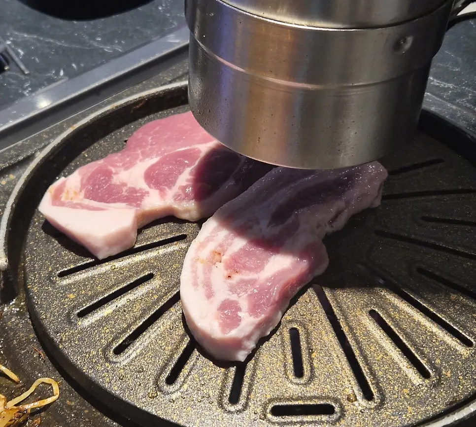 A plate of meat grilling alongside minari and kimchi