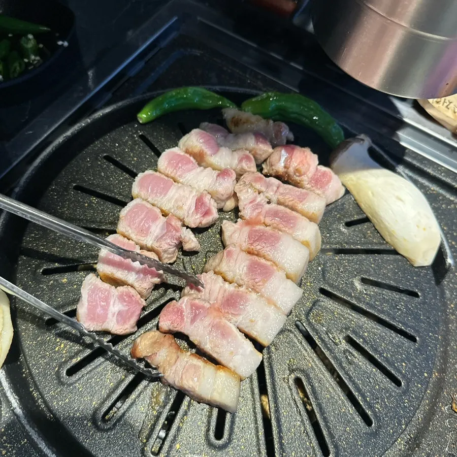 A staff member grilling thick slices of pork belly on the grill