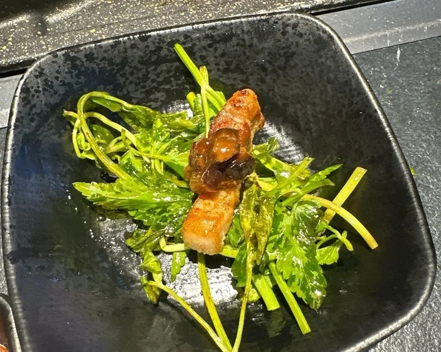 Chopsticks holding minari and pork belly together