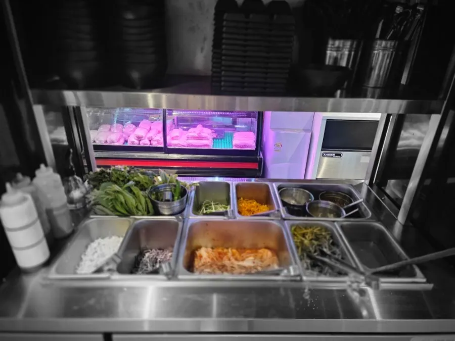 Self-serve side dish bar with lettuce, perilla leaves, bean sprouts, and kimchi refills