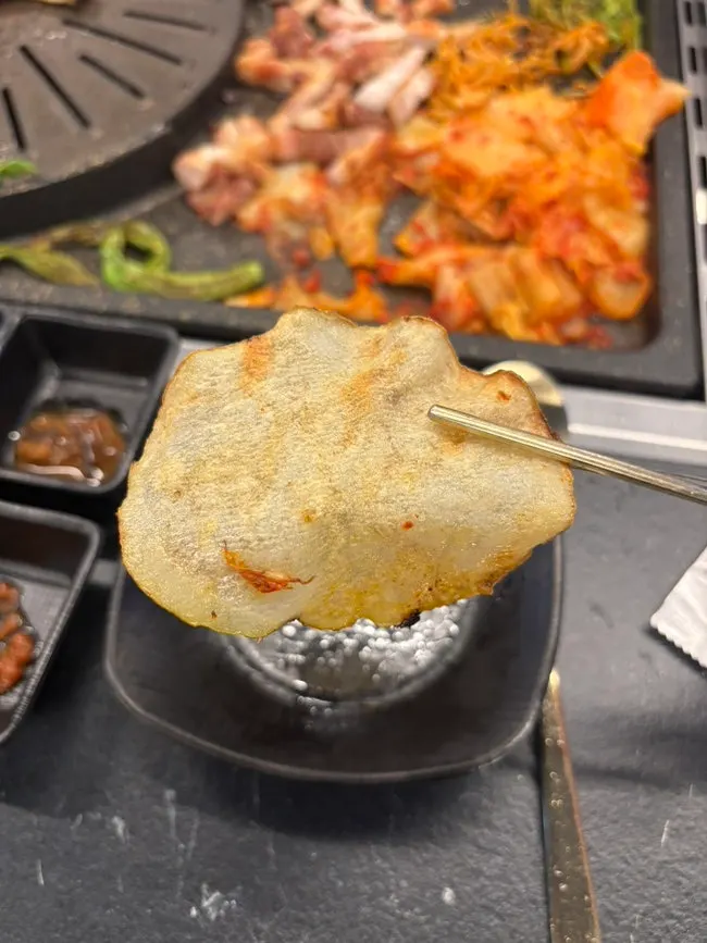 A potato slice wrap topped with mushroom wasabi and garlic scapes