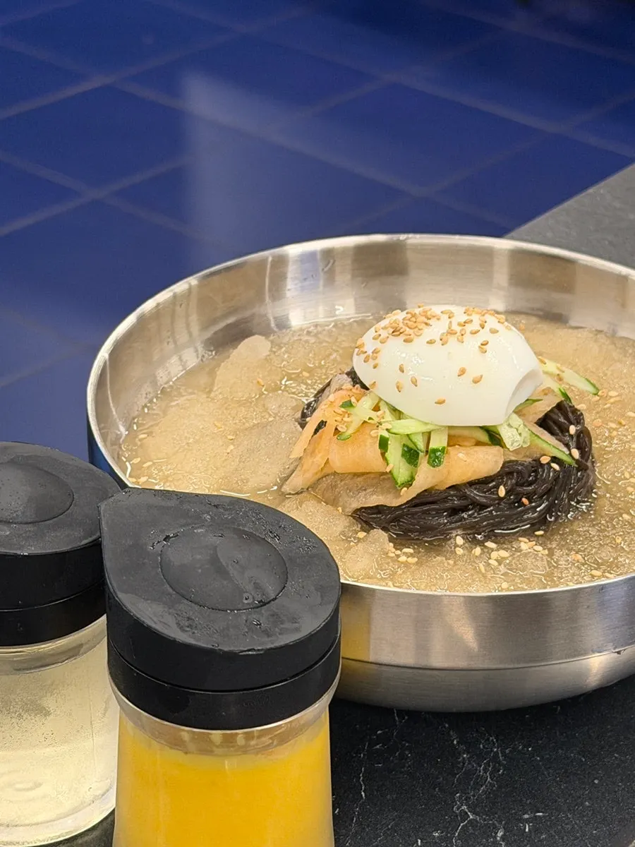 A bowl of cold noodles with ice flakes floating on top