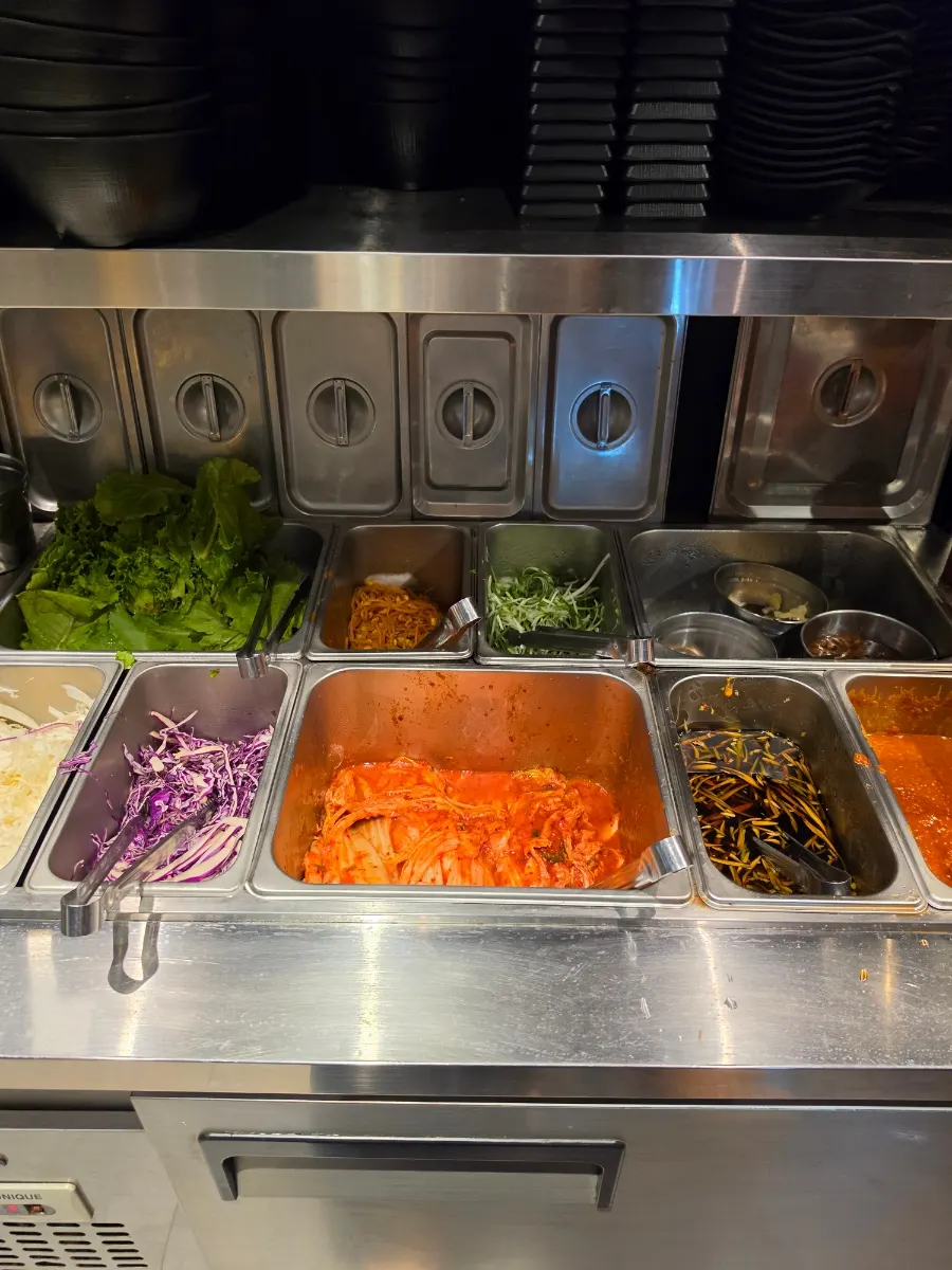 Self-serve side dish corner with lettuce, scallion strips, and kimchi