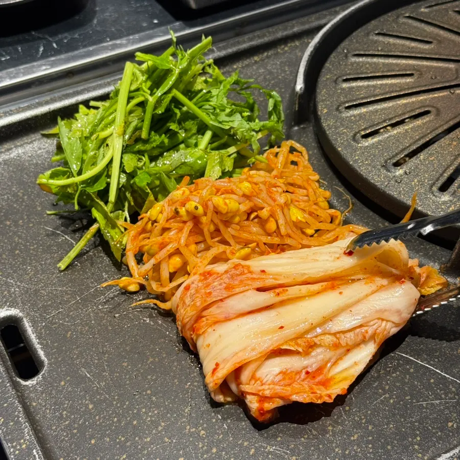 Minari, seasoned bean sprouts, and sliced potato grilling beside the meat