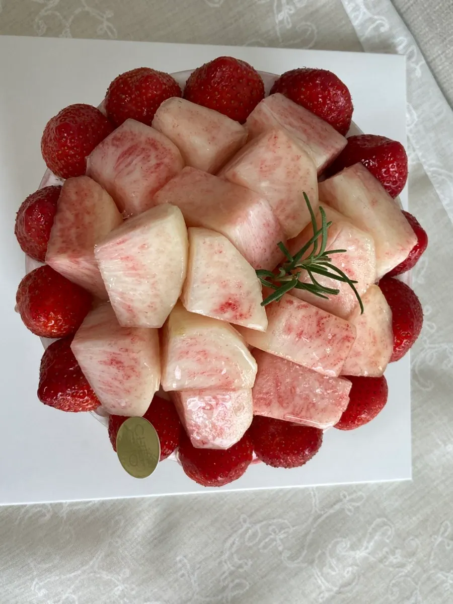 The cake's top surface densely covered in strawberries and peaches over whipped cream