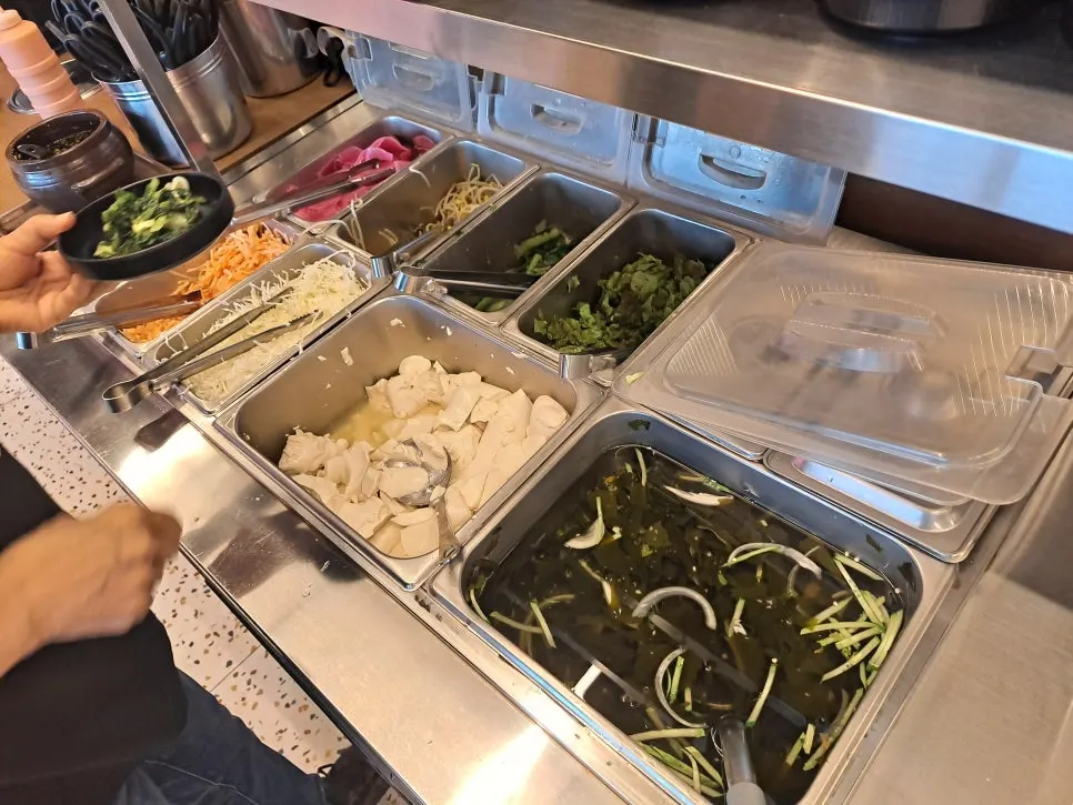 Banchan and bibimbap ingredients laid out at the self-serve bar
