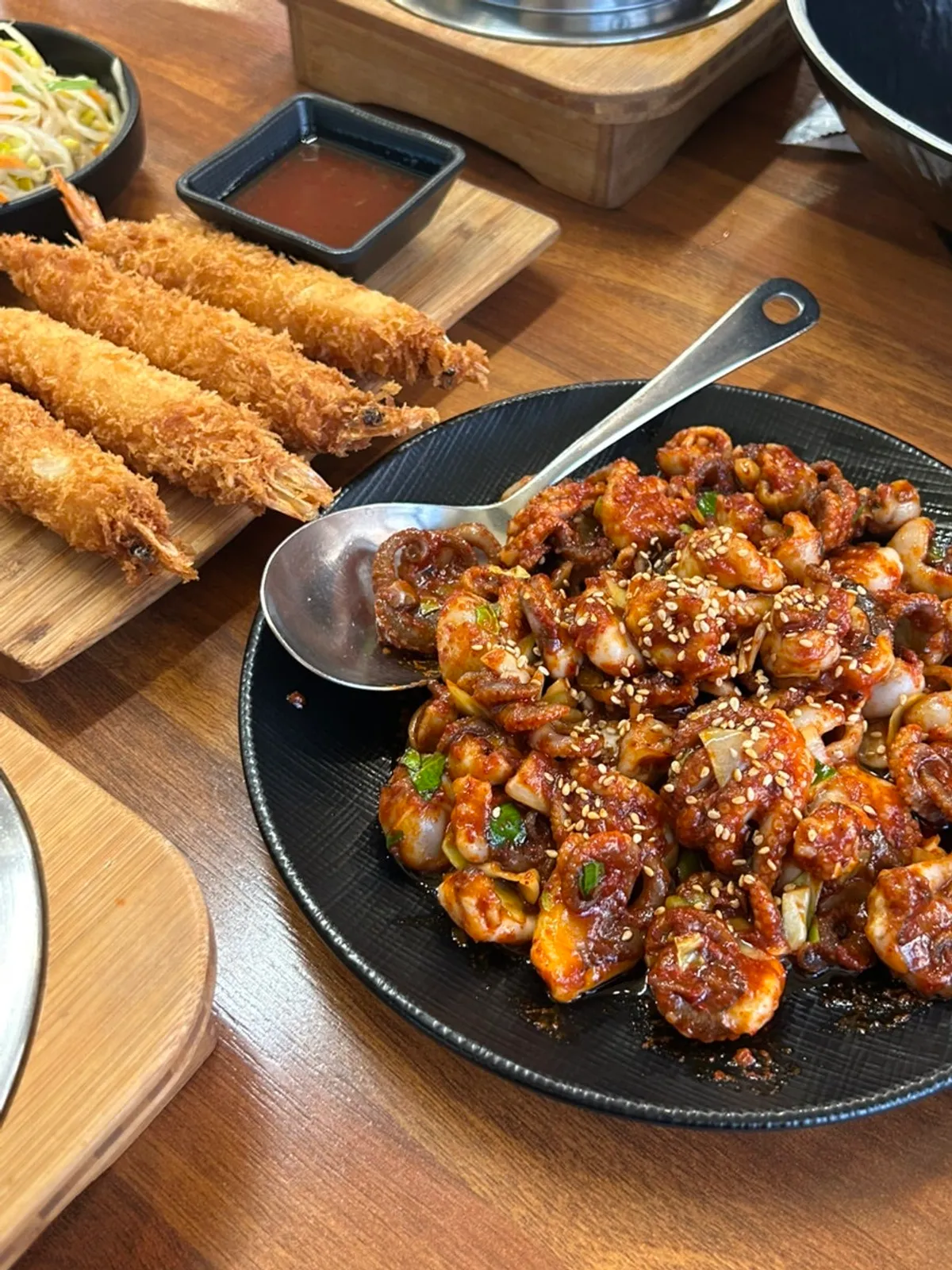 Mesa servida con jjukkumi salteado, sotbap y camarones fritos