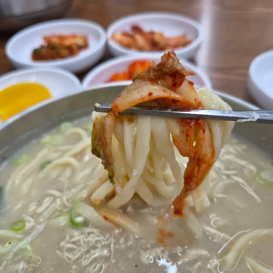 A chopstick lifting noodles with kimchi piled on top