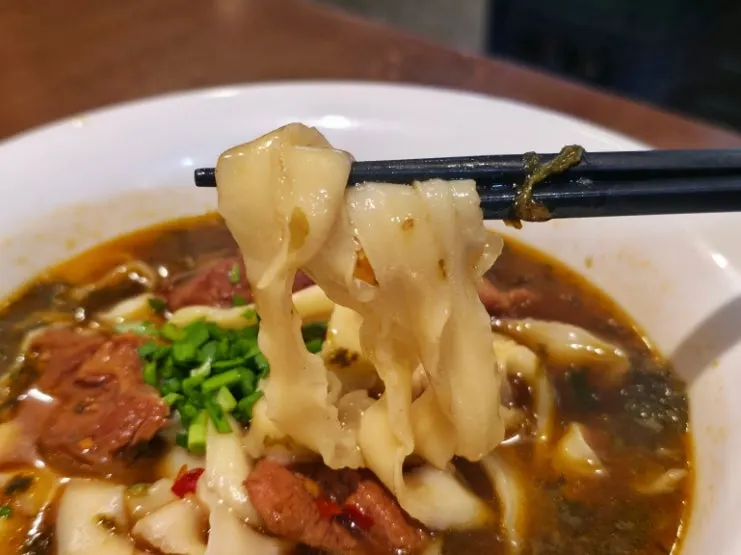 Lifting up a forkful of beef knife-cut noodles