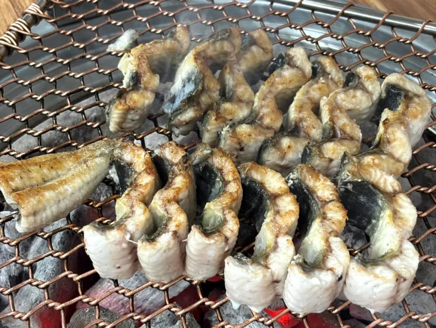Thick cuts of grilled eel cooking on the grill plate