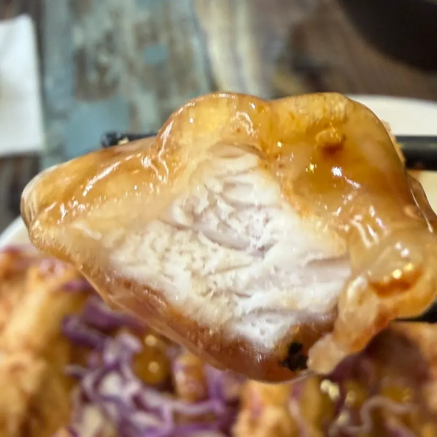A piece of sweet-and-sour pork lifted with chopsticks