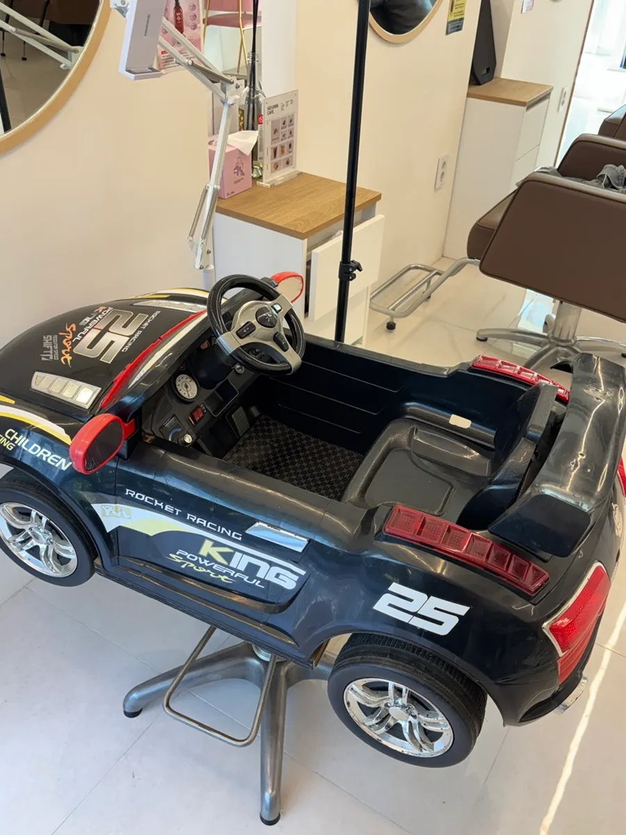 A kids' car-shaped chair placed in a corner of the salon