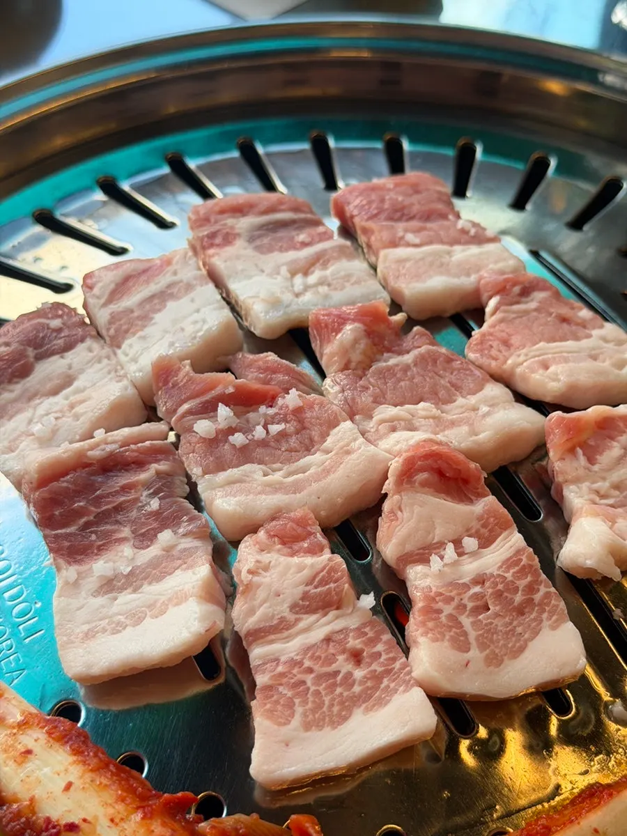 Well-lit charcoal grill with pork belly on top