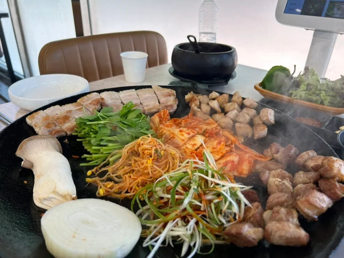 Pork belly, neck, and jowl grilling together with minari and kimchi on the pot lid