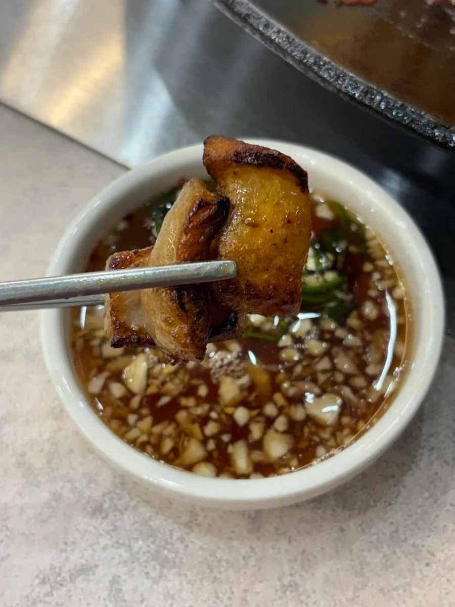 A piece of pork belly lifted off the hot pot lid