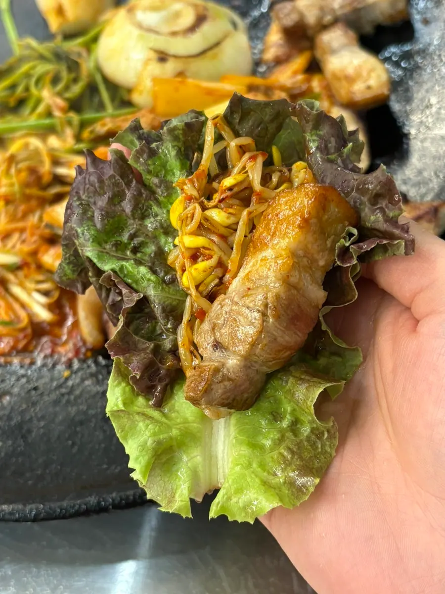 A wrap of pork neck with grilled kimchi and minari