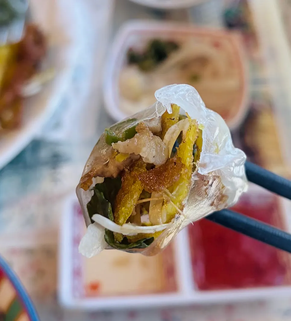 A rice-paper-wrapped banh xeo roll dipped in sauce