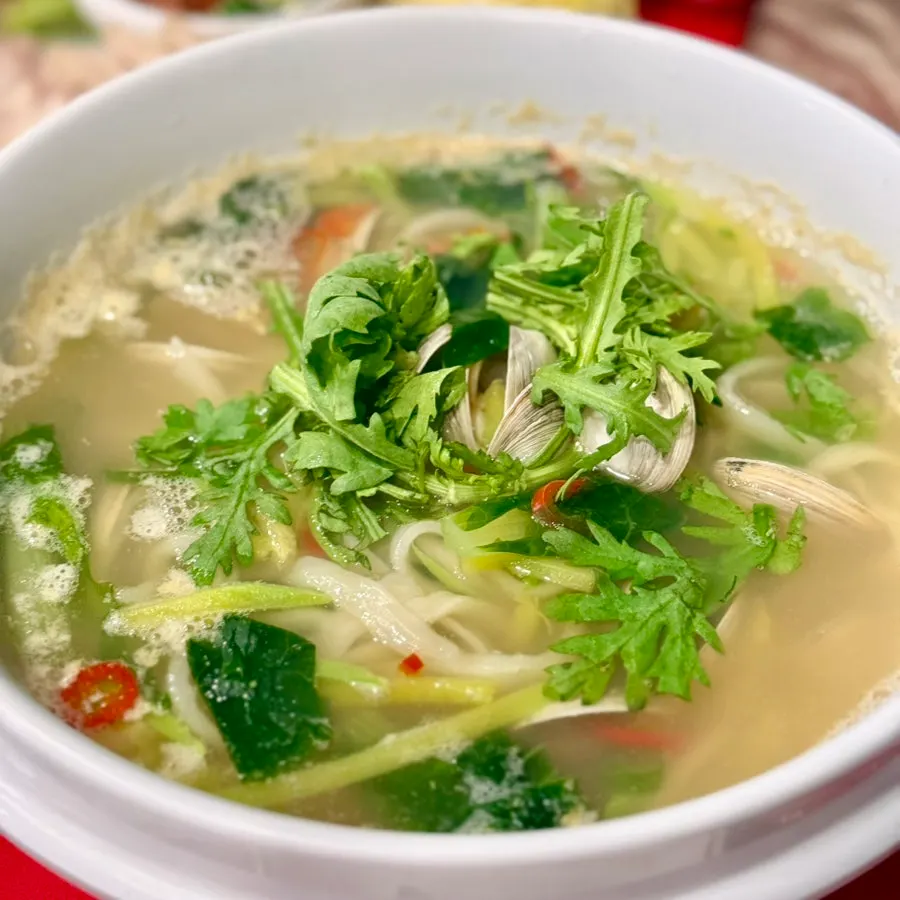 Broth of clam noodle soup topped with crown daisy greens