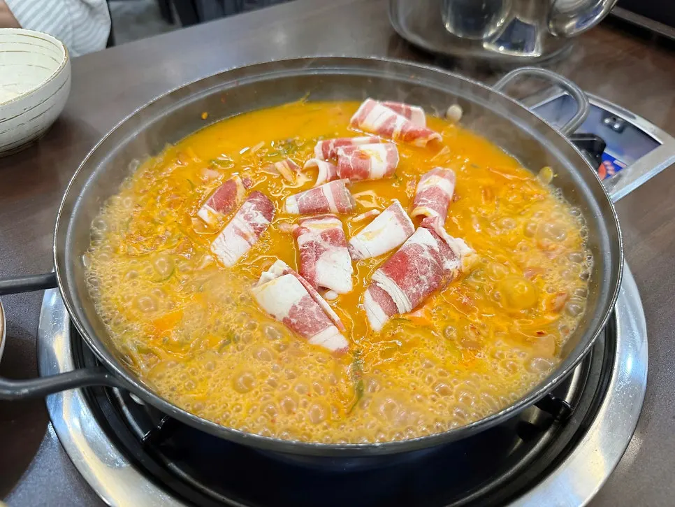 A bowl of rice topped with ham and vegetables with broth poured over