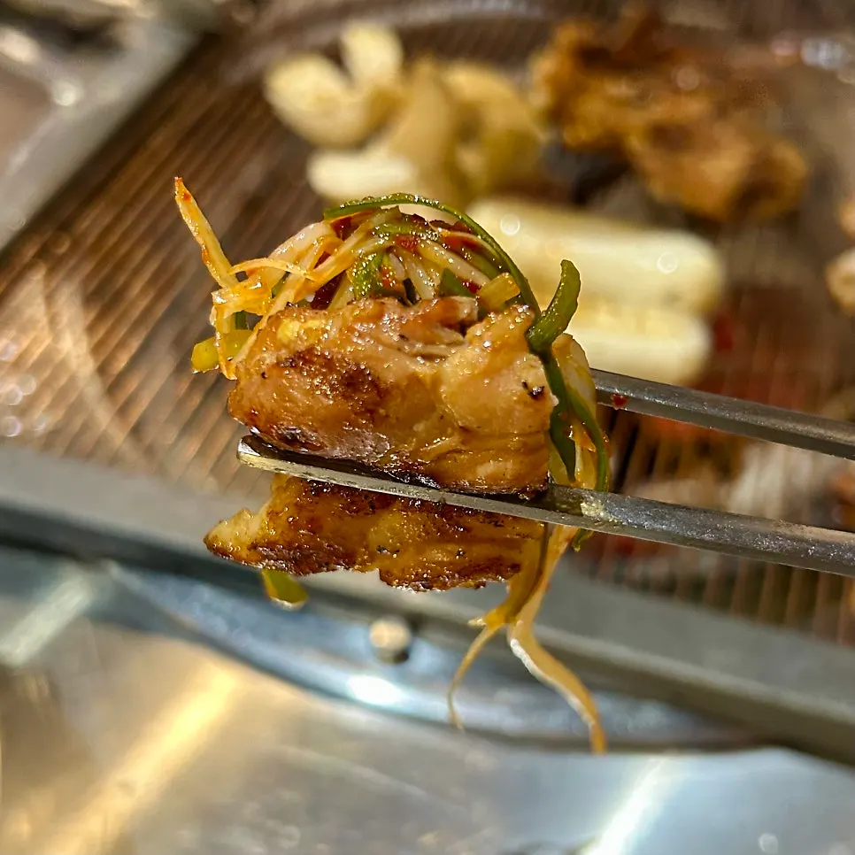 A bite of charcoal chicken galbi with pickled radish and shredded green onion