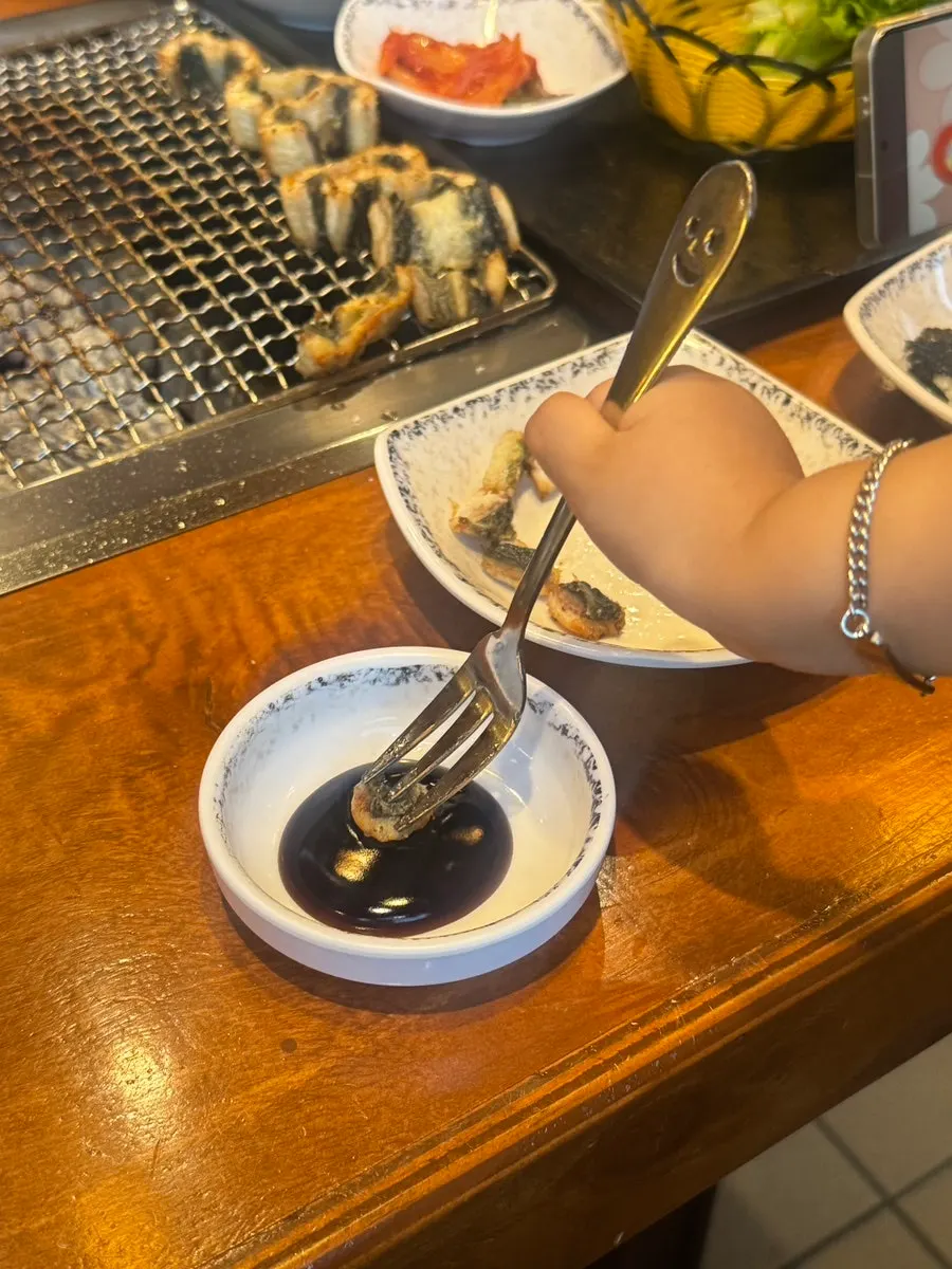 The toddler picking up a piece of eel to eat