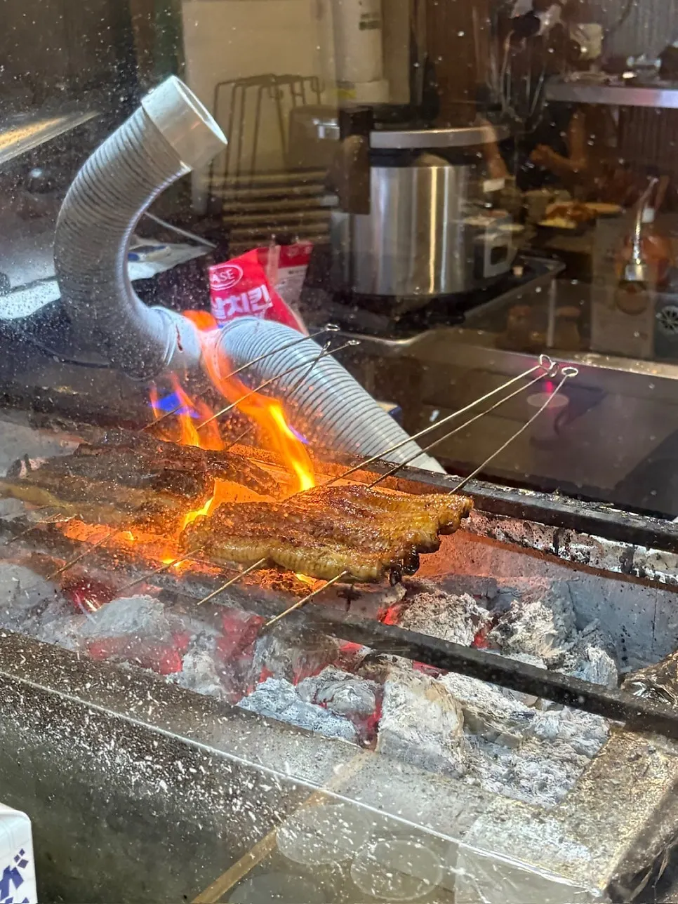 Eel grilling over binchotan charcoal seen through the kitchen glass
