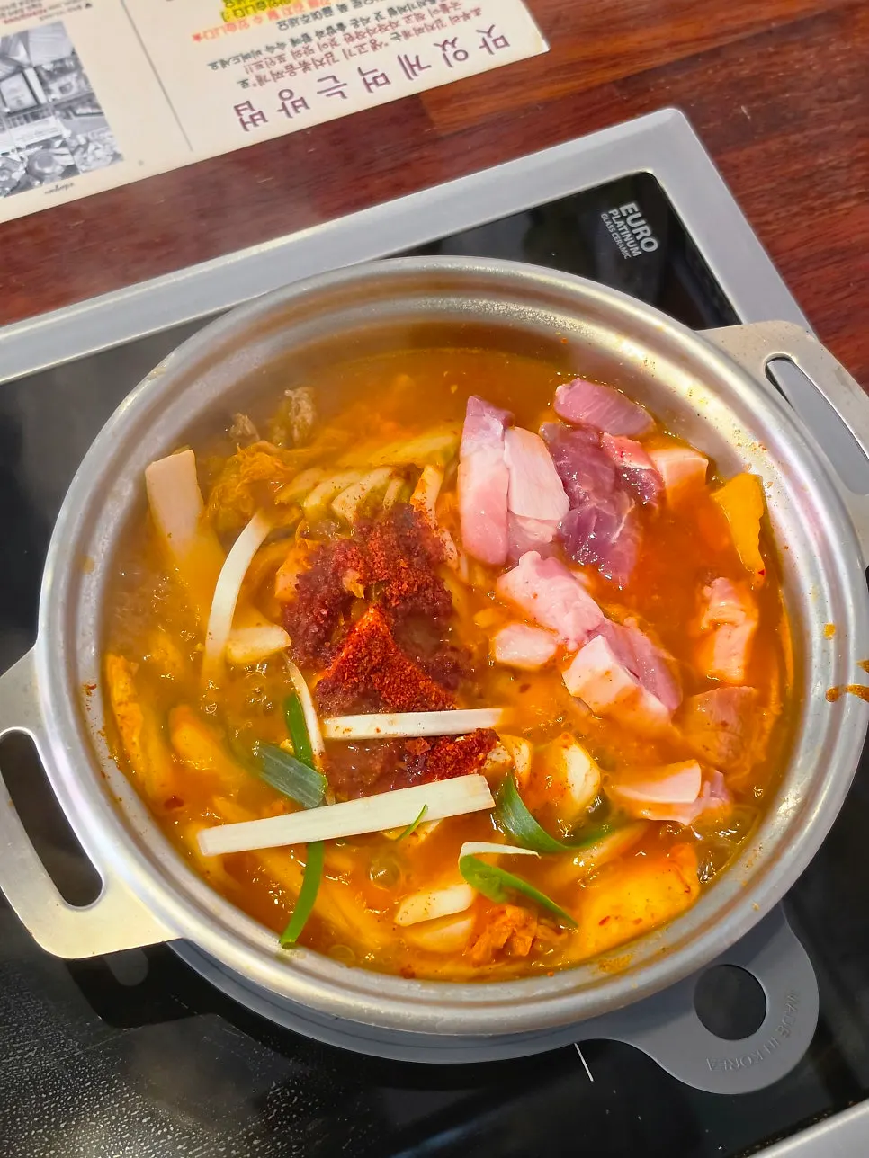 Pot of kimchi jjigae topped with raw pork