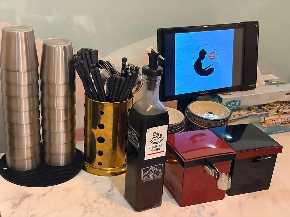 Table set with a water cup, utensils, soy sauce, pickled ginger, and takuan