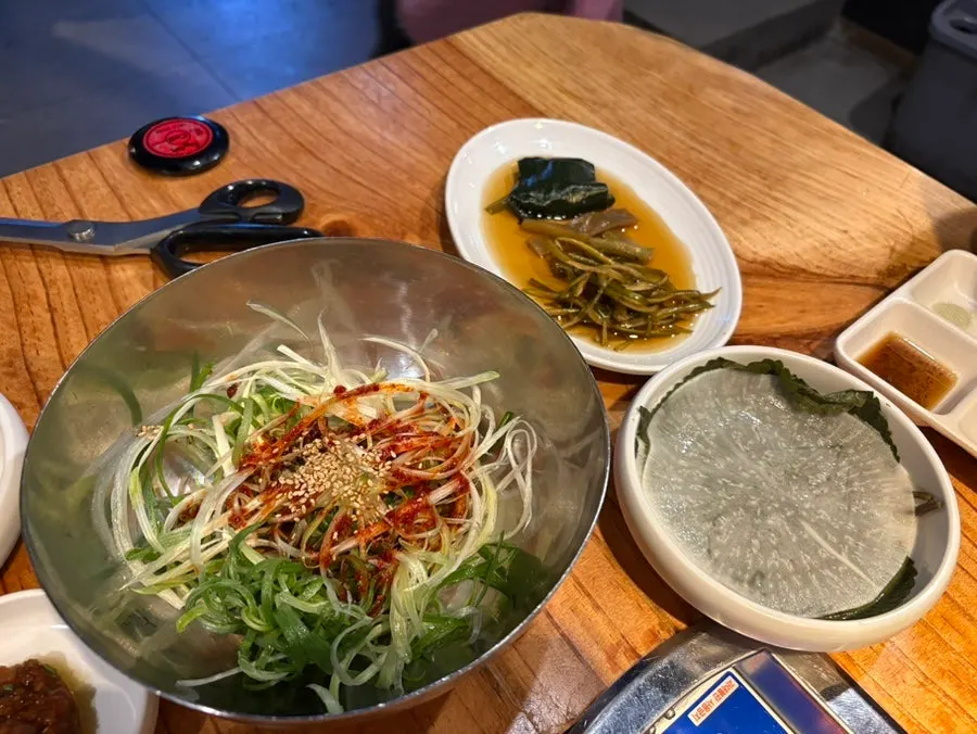 A spread of shredded green onion, pickled radish, and pickles side dishes