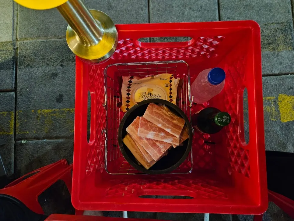 Water, soju, and wet wipes held in a red milk crate next to the table
